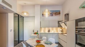 A modern kitchen with white cabinets, a built-in oven, and a dining area with a marble table and white chairs.