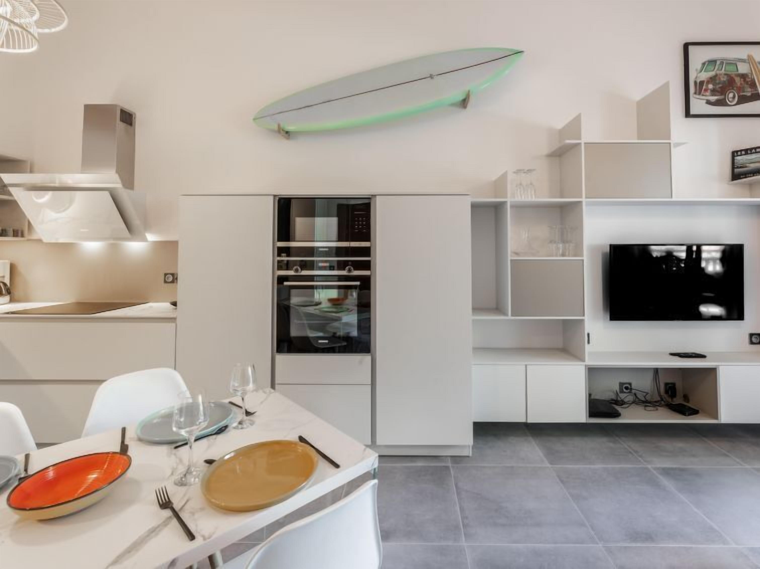 Une cuisine moderne avec des meubles blancs, un four encastré et un coin repas avec une table dressée pour deux personnes.