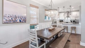 A modern kitchen with white cabinetry, a wooden dining table, and a chandelier. - Newly Redesigned, Steps to Lagoon Pool and Beach (Rosemary Beach)
