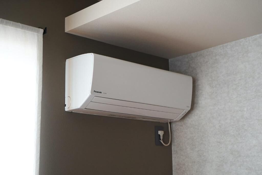 Eine weiße Klimaanlage an einer Wand in einem Raum mit Fenster und einer Wand mit Grau-Struktur.