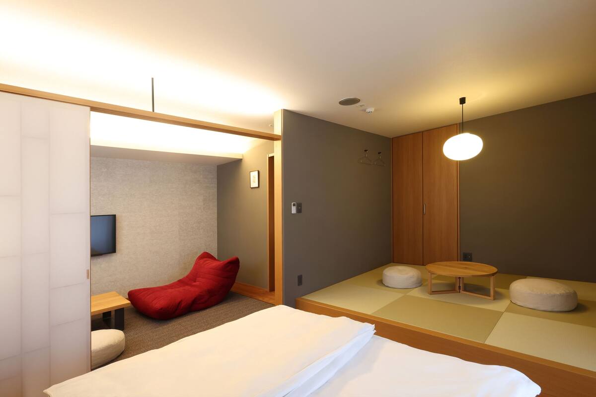 A modern hotel room with a bed, a red bean bag, a small table, and a television.
