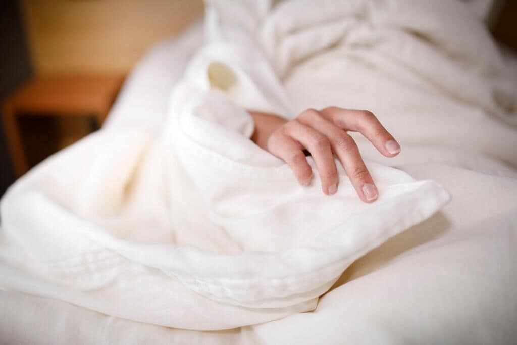 A person sitting on a bed with a white blanket.