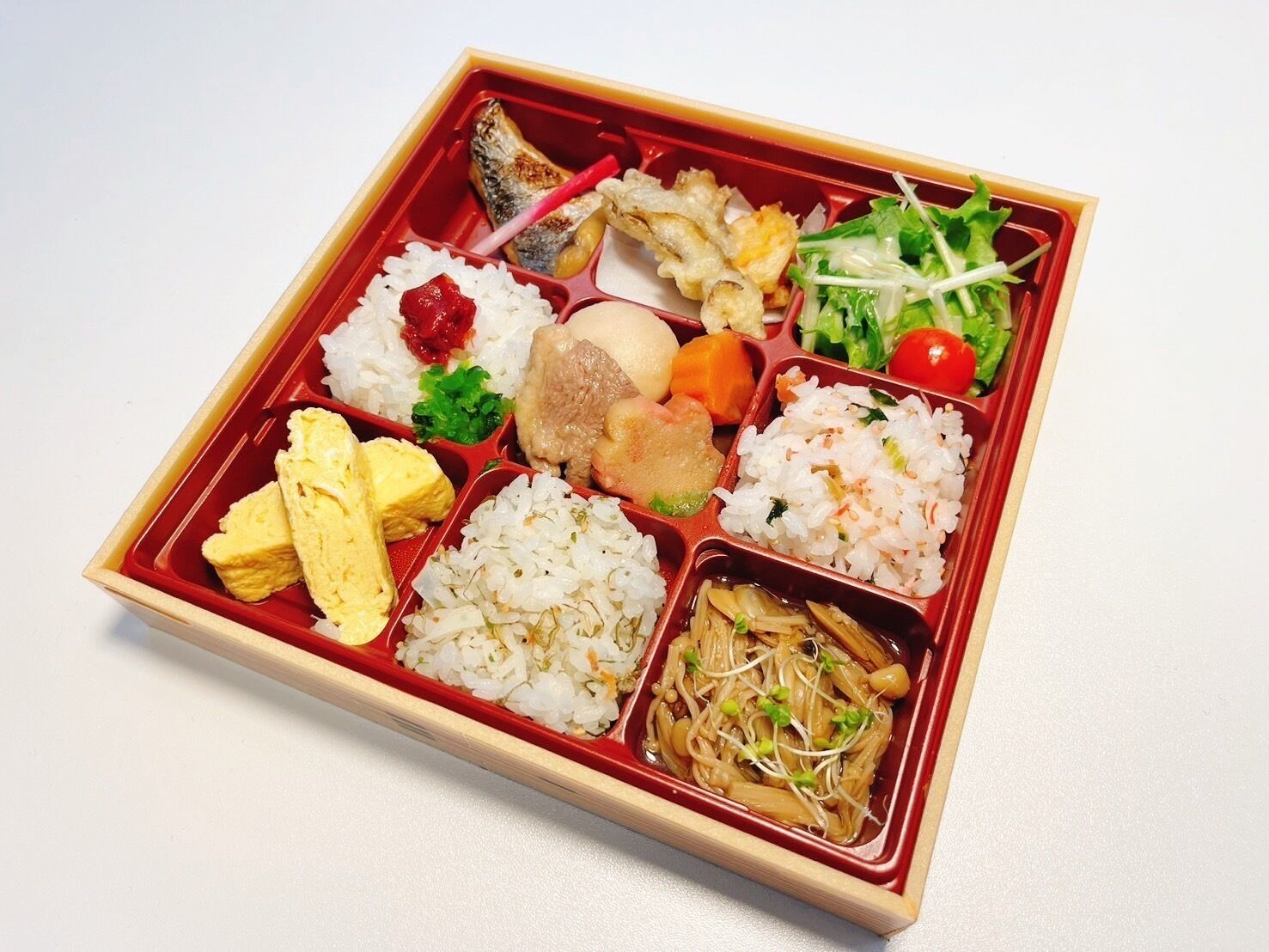 Una caja bento con diversos alimentos, como arroz, pescado, verduras y huevo.