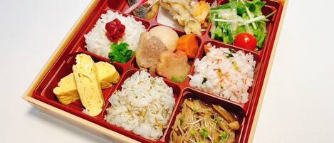 Una caja bento con diversos alimentos, como arroz, pescado, verduras y huevo.