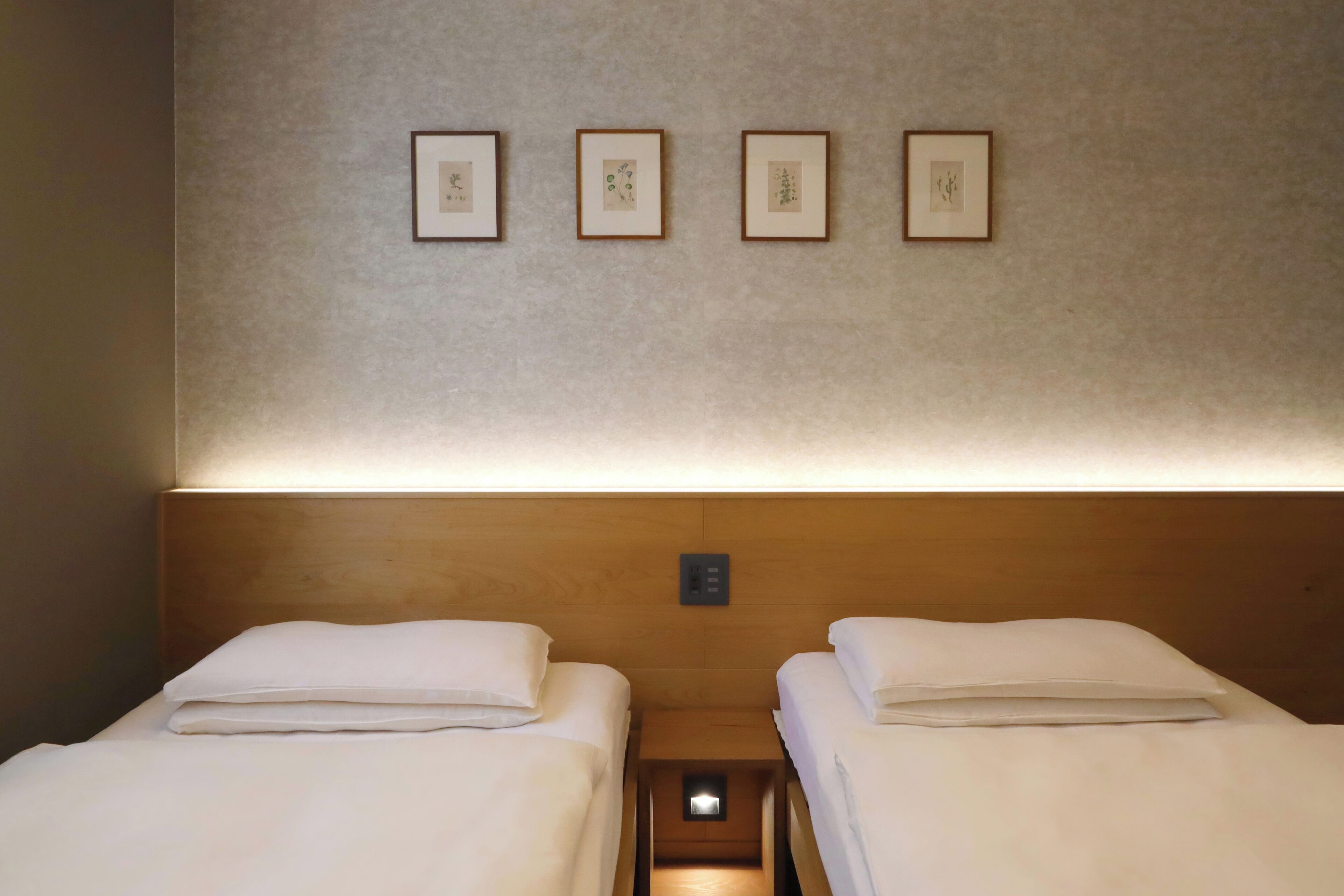 A hotel room with two single beds, a wooden headboard, and four framed botanical prints on the wall.