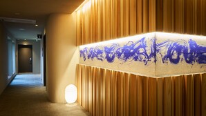 A hallway with a wooden panel wall, a textured light fixture, and a carpeted floor. - NEON HOTEL (Kanazawa)