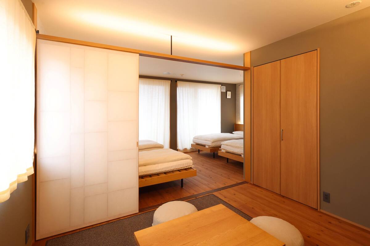 A compact hotel room with two single beds, a wooden wardrobe, a small table, and a sliding door.