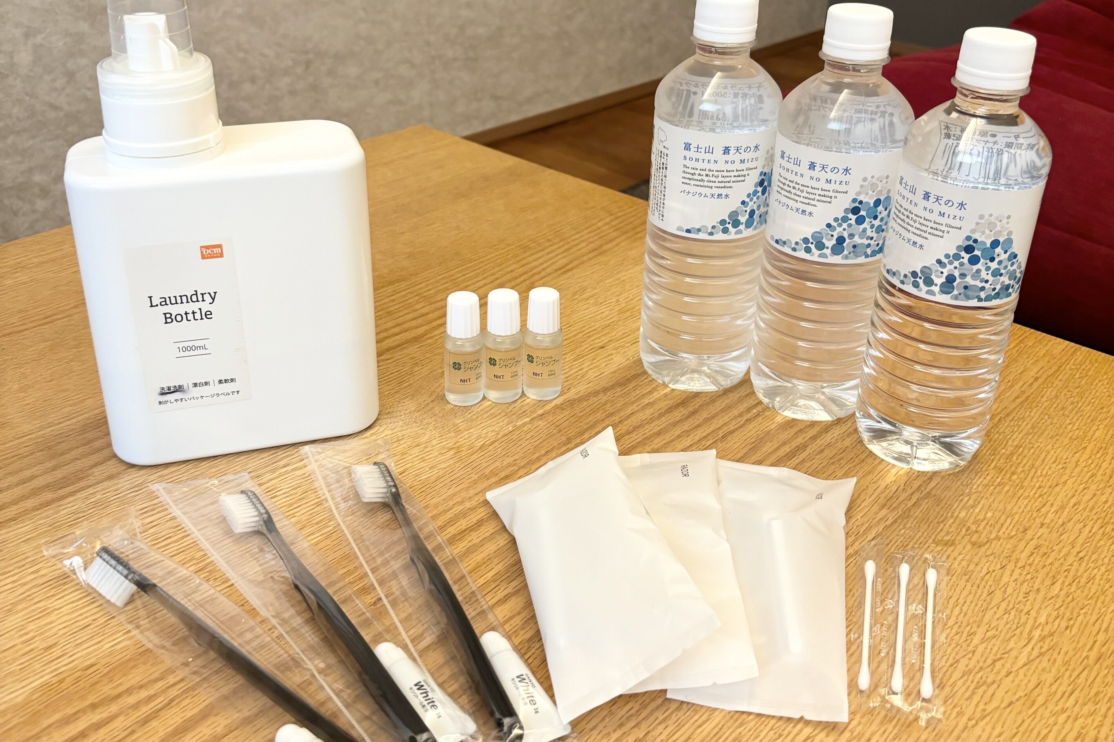 A table with a large white bottle labeled "Laundry Bottle 1000mL," three clear bottles with blue labels, several toothbrushes, cotton swabs, and white cloth packets.