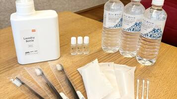A table with a large white bottle labeled "Laundry Bottle 1000mL," three clear bottles with blue labels, several toothbrushes, cotton swabs, and white cloth packets.