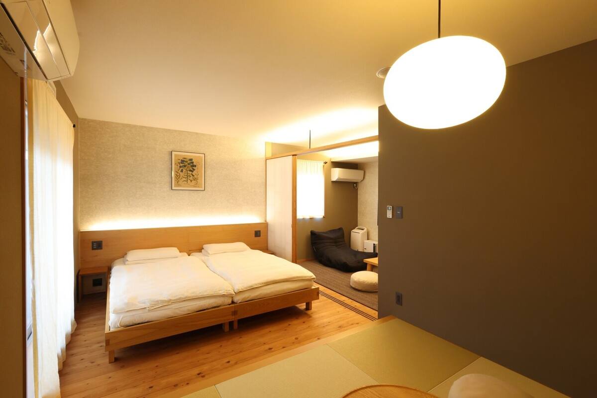 A bedroom with a wooden bed, a bedside table, a mirror, and a wall-mounted air conditioner.