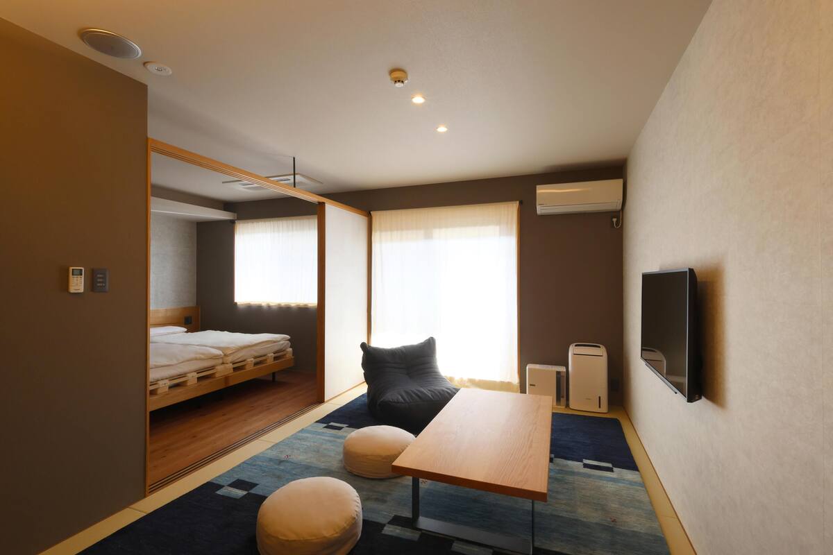 A compact hotel room with a bed, a sofa, a small table, and a TV.