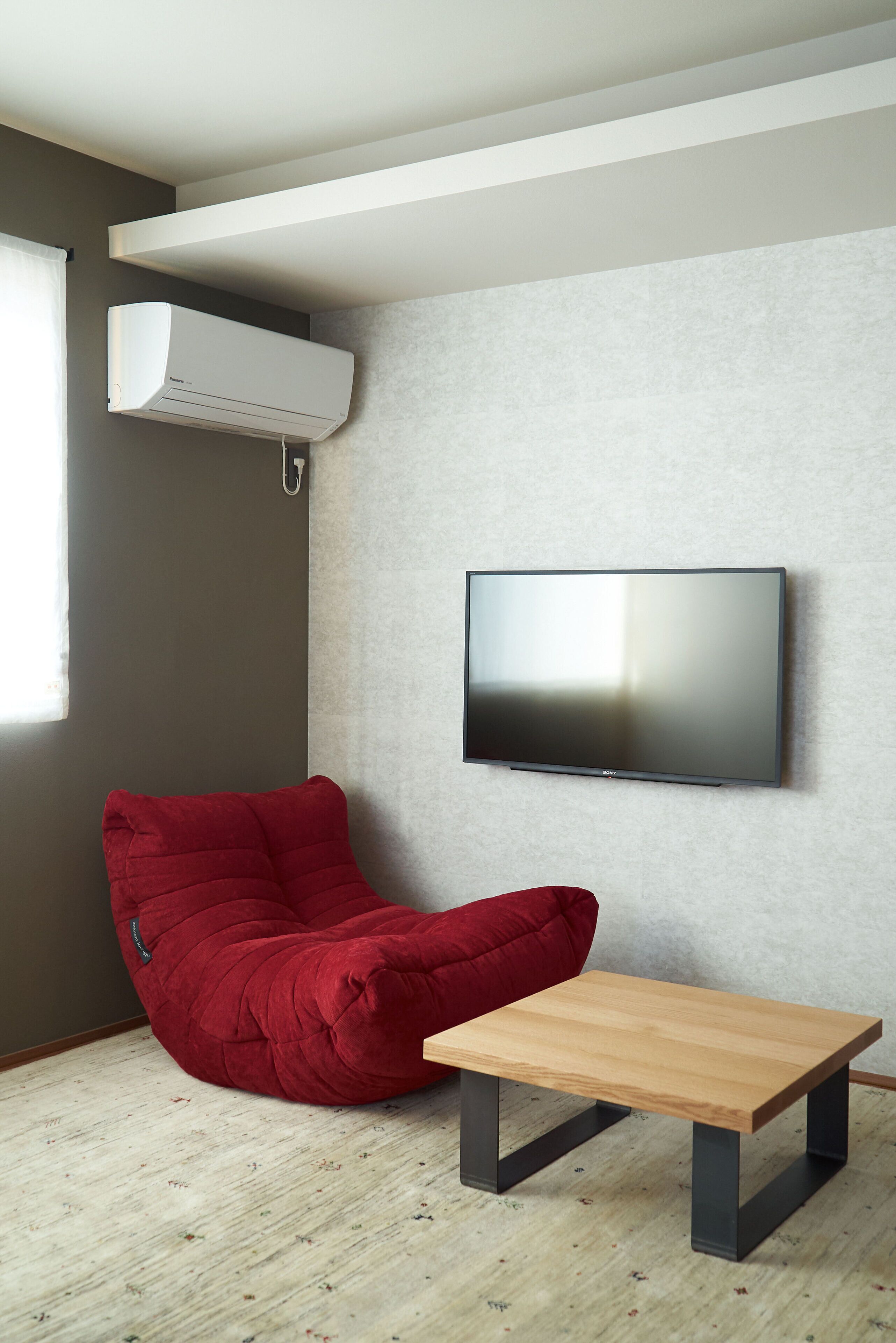 Un soggiorno moderno con una TV a schermo piatto montata a parete, una poltrona sacco rossa e un tavolino da caffè in legno.