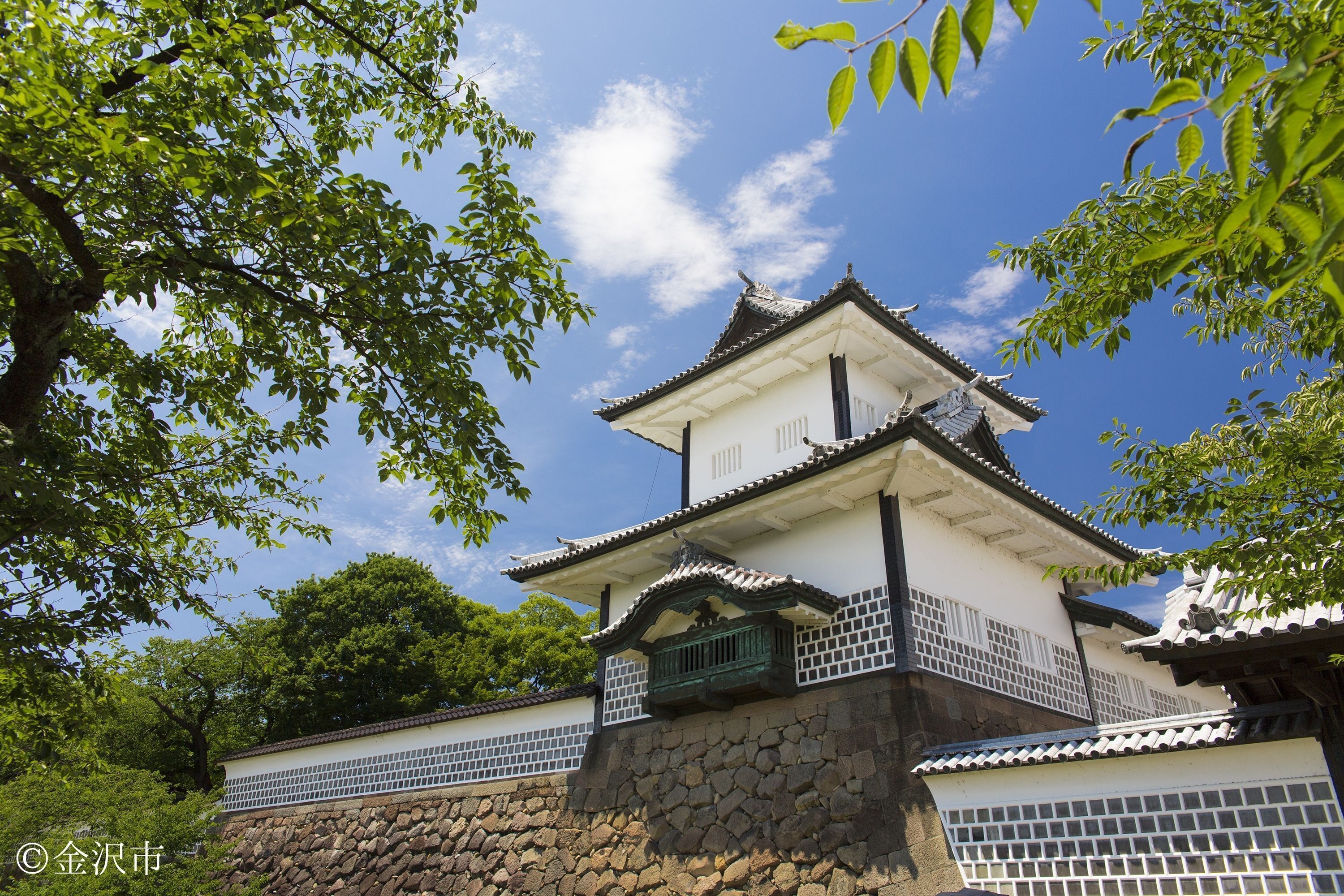 Un castillo japonés tradicional, con base de piedra y paredes blancas, rodeado de abundante vegetación.