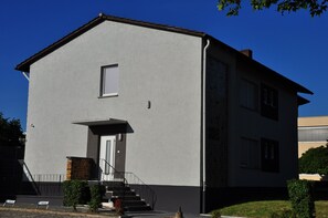 A two-story building with a flat roof, a small window on the upper floor, and a front door with a small porch. - Weisenau Plaza (Mainz)