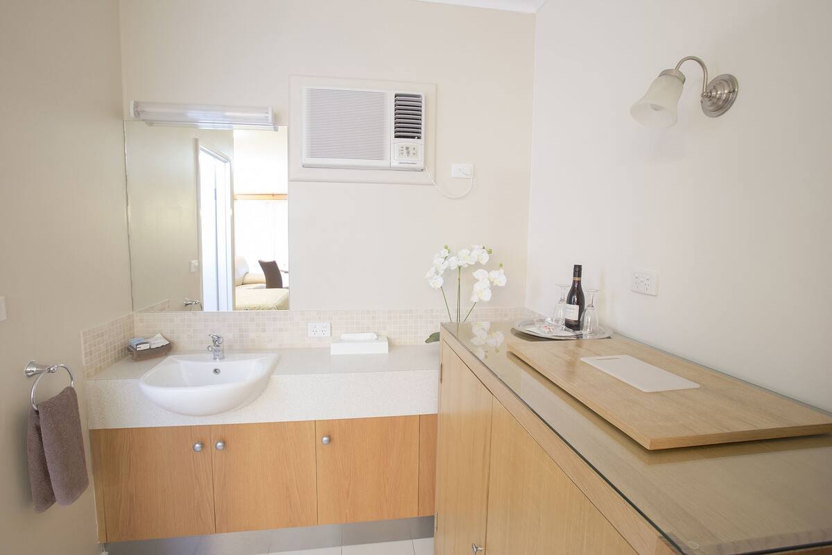 A modern bathroom with a double sink, wooden cabinets, a mirror, an air conditioning unit, and a wall-mounted light fixture.