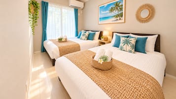 Une chambre d’hôtel avec deux lits, une fenêtre avec des rideaux, un climatiseur fixé au mur, un tableau encadré représentant une plage et un miroir décoratif mural.