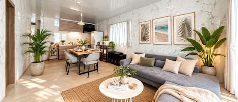 En moderne stue med en grå sofa, et spisebord og et køkken i baggrunden.
