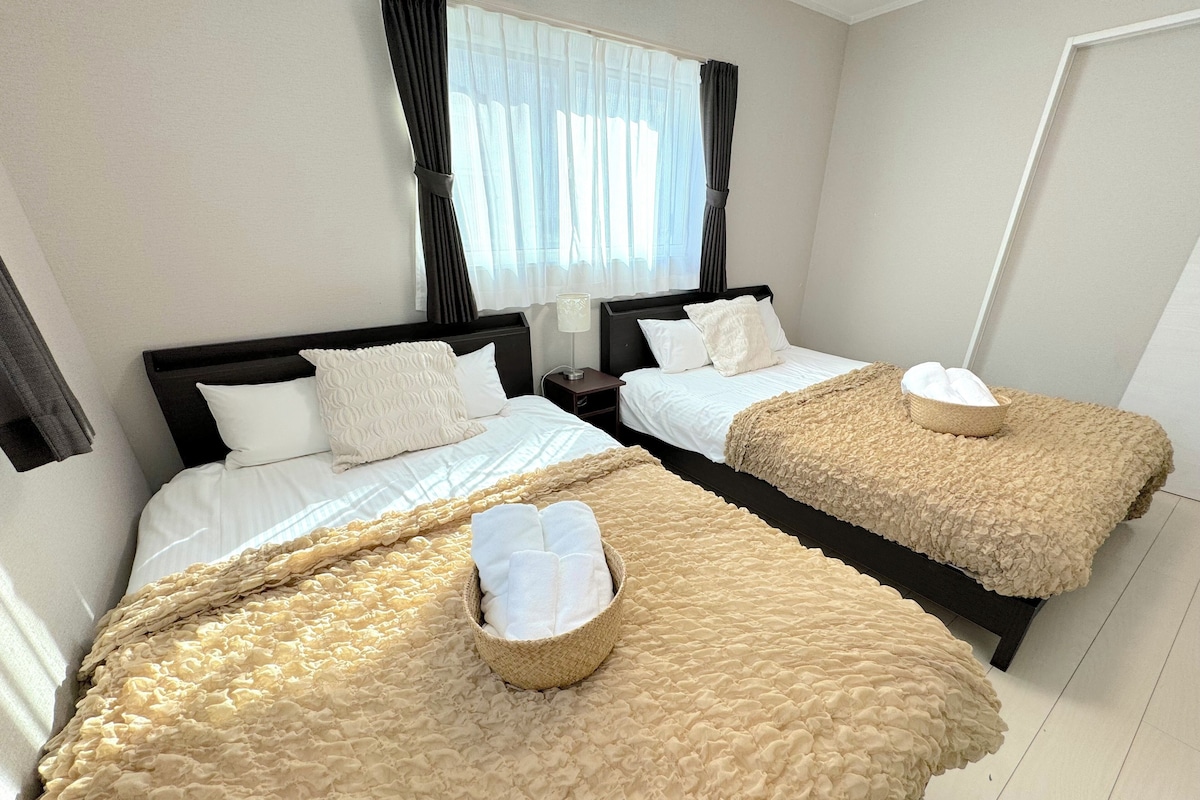A hotel room with two beds, each with a textured beige blanket and a woven basket on the bed.