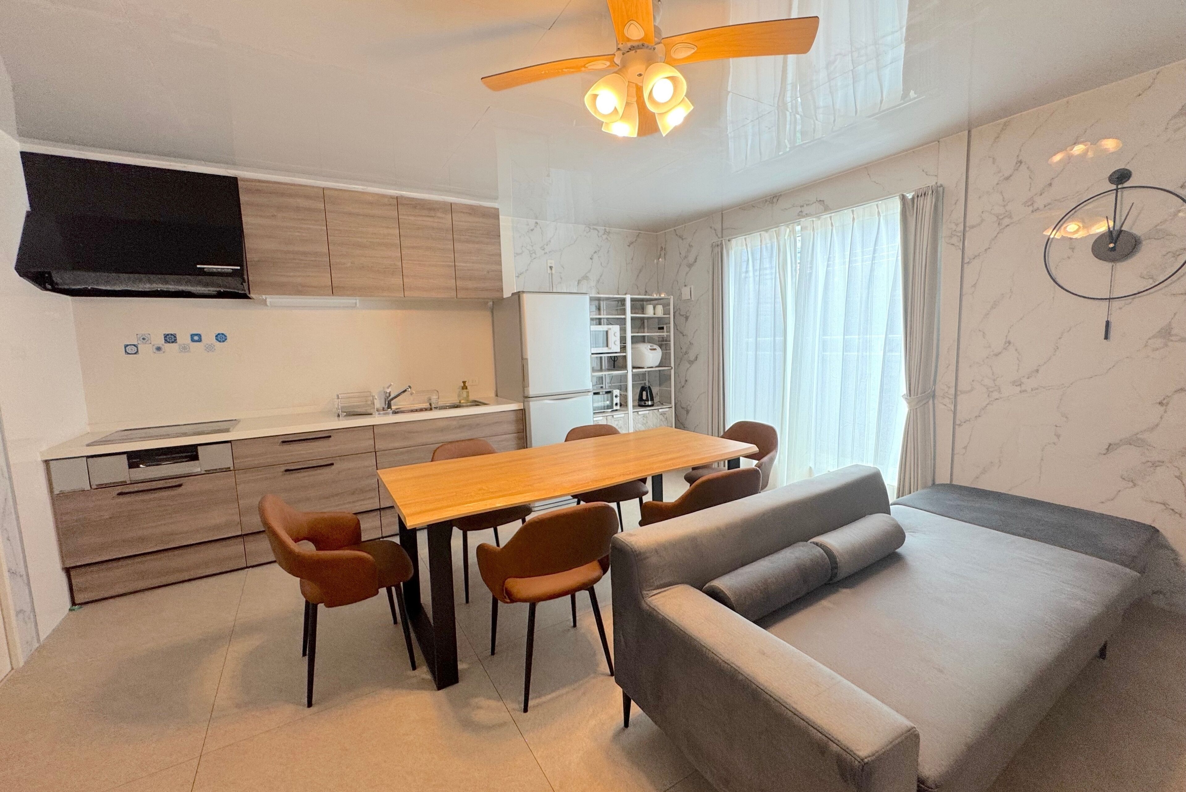 A modern kitchen with a dining area, a sofa, and a ceiling fan.
