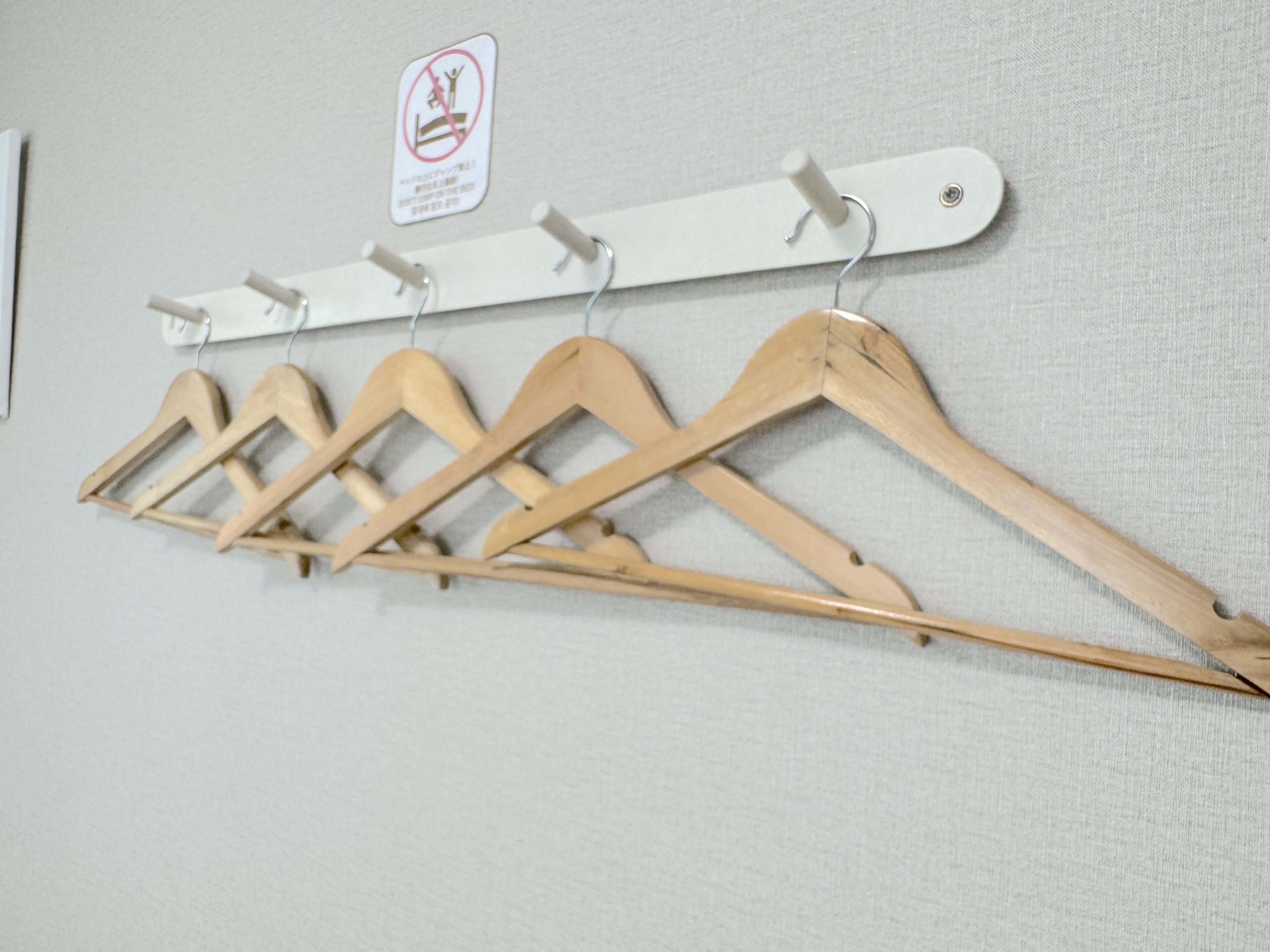 A wall-mounted wooden hanger rack with five hangers against a textured wall.