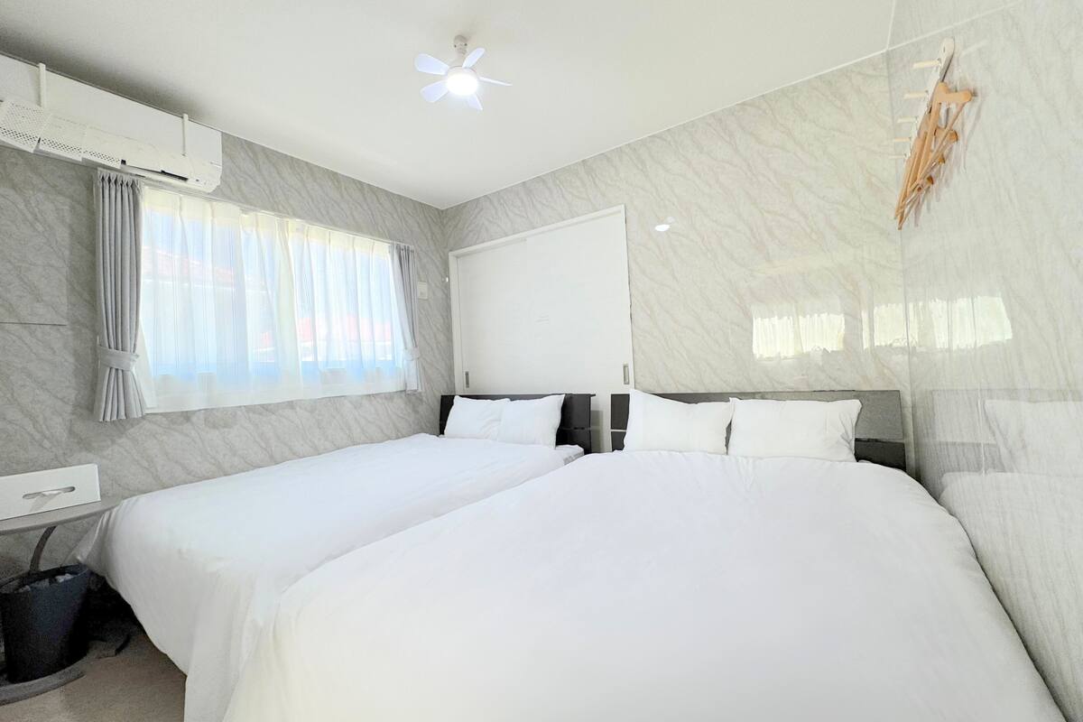 Une chambre d’hôtel avec deux lits, un ventilateur de plafond, un appareil de climatisation, une fenêtre avec des rideaux et un téléviseur fixé au mur.