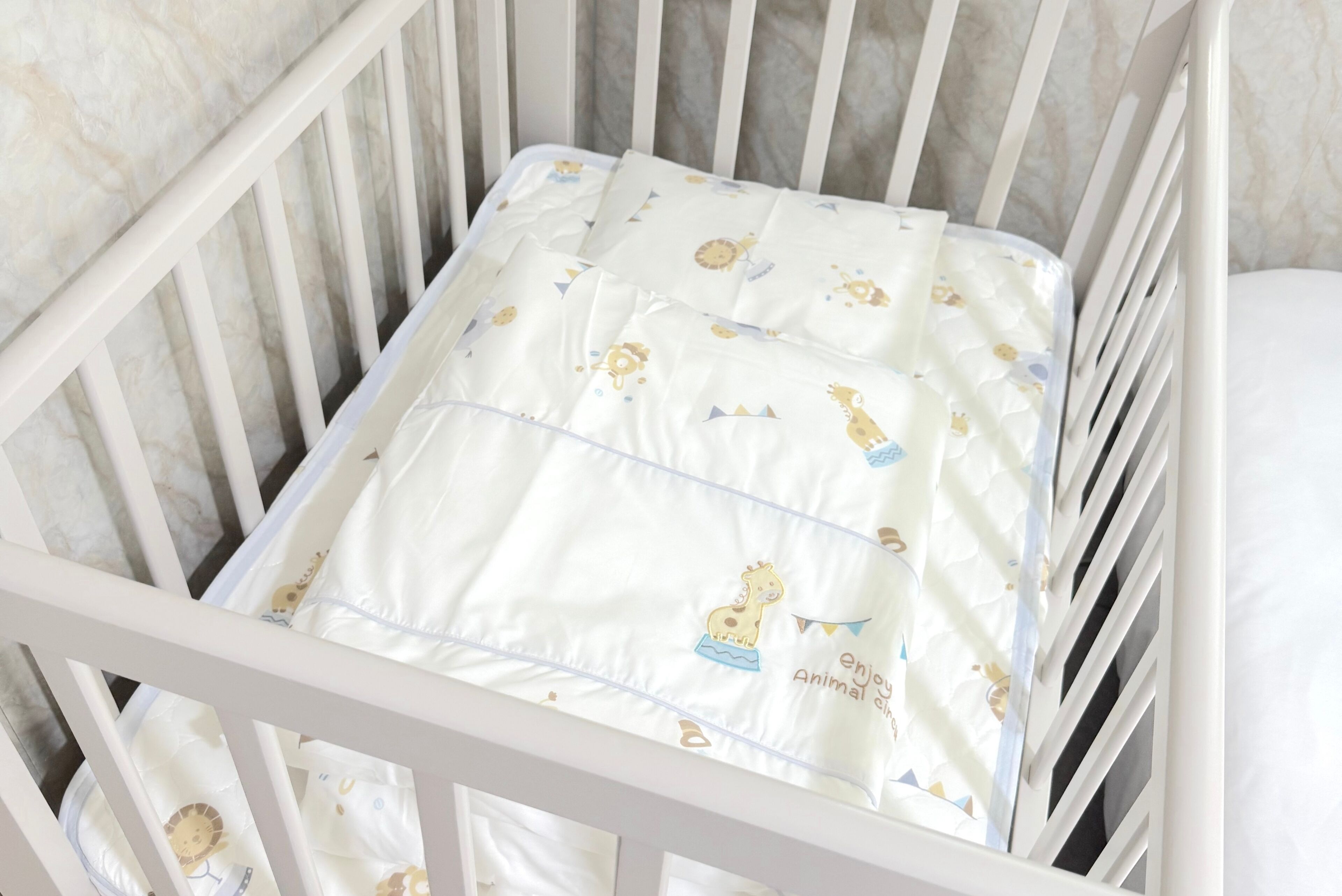 Una cuna con colchón blanco decorado con estampados de animales y el texto "enjoy Animal change".