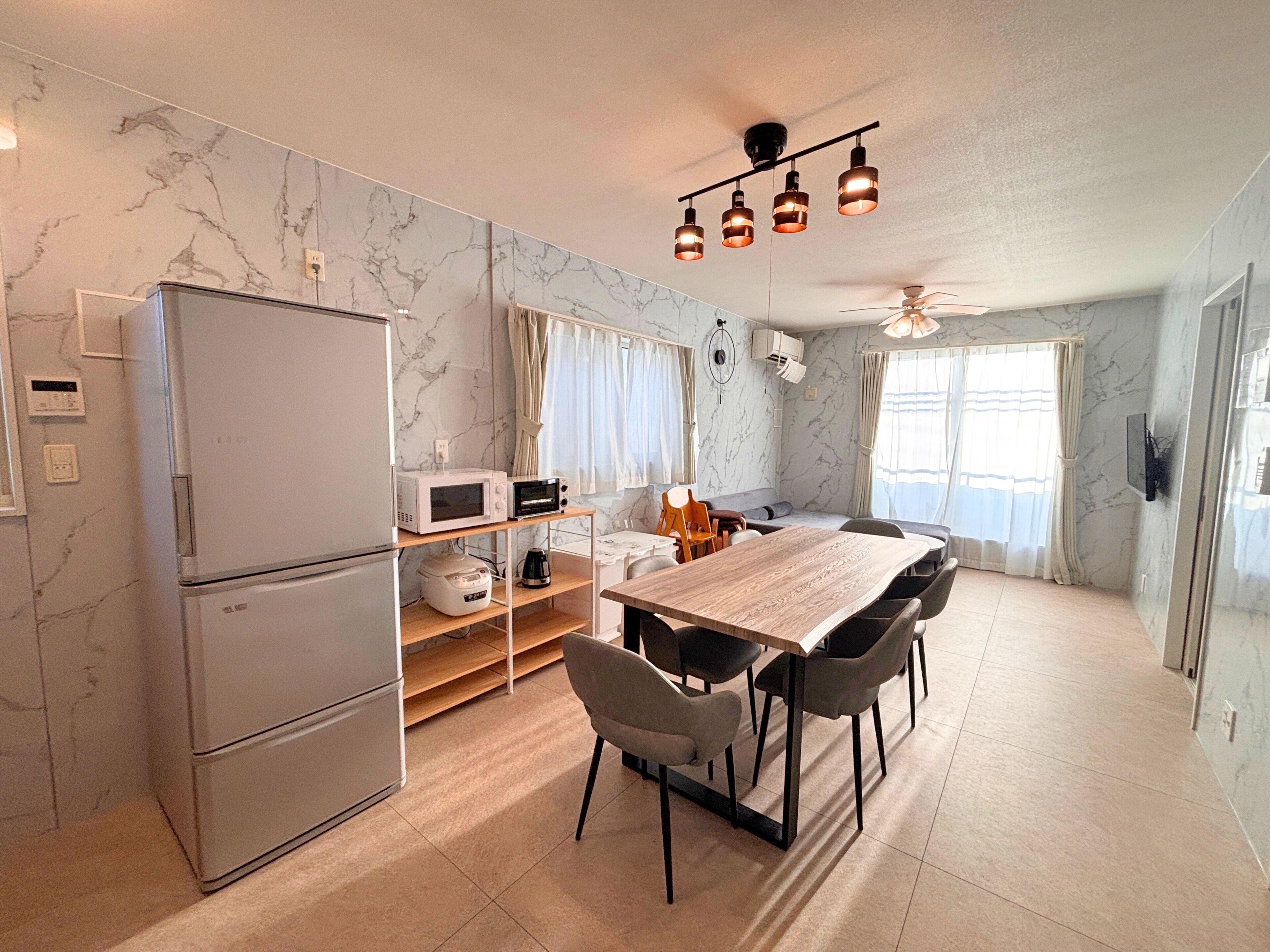 Eine kompakte Küche mit einem Kühlschrank, einer Mikrowelle und einer Kaffeemaschine auf einem Regal, einem Esstisch mit Stühlen und einem Deckenventilator.