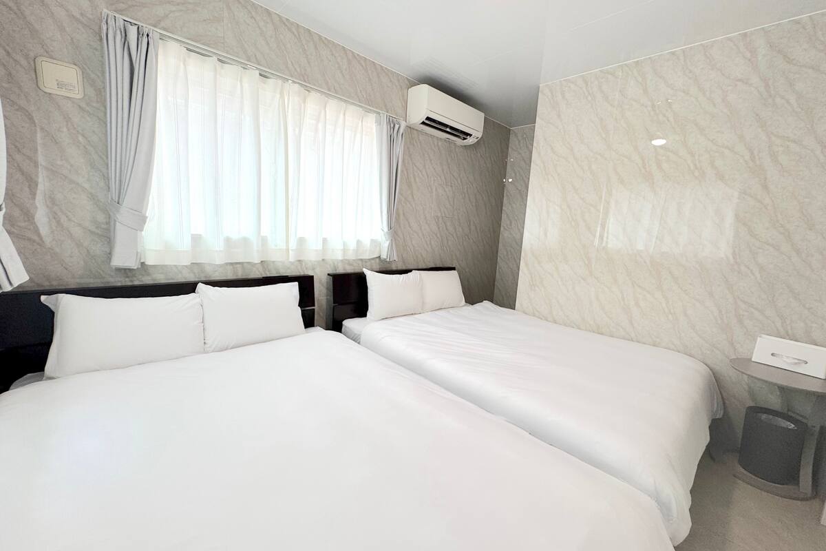 Une chambre d’hôtel avec deux lits, une fenêtre avec des rideaux, un appareil de climatisation et un mur en marbre.