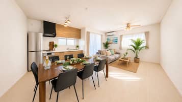 A modern kitchen with a dining area, a living room with a sofa, and a ceiling fan.