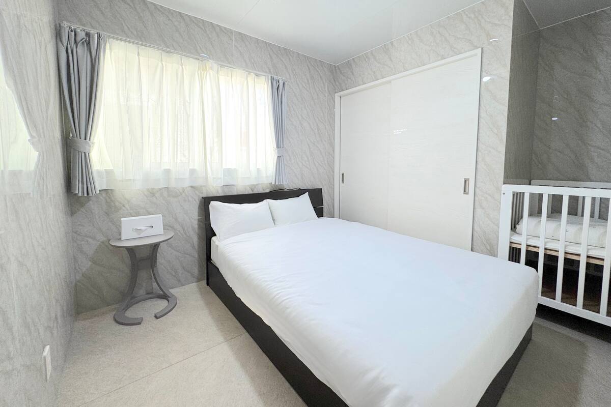 Une chambre à coucher moderne avec un grand lit, une petite table de chevet, un berceau et une armoire.