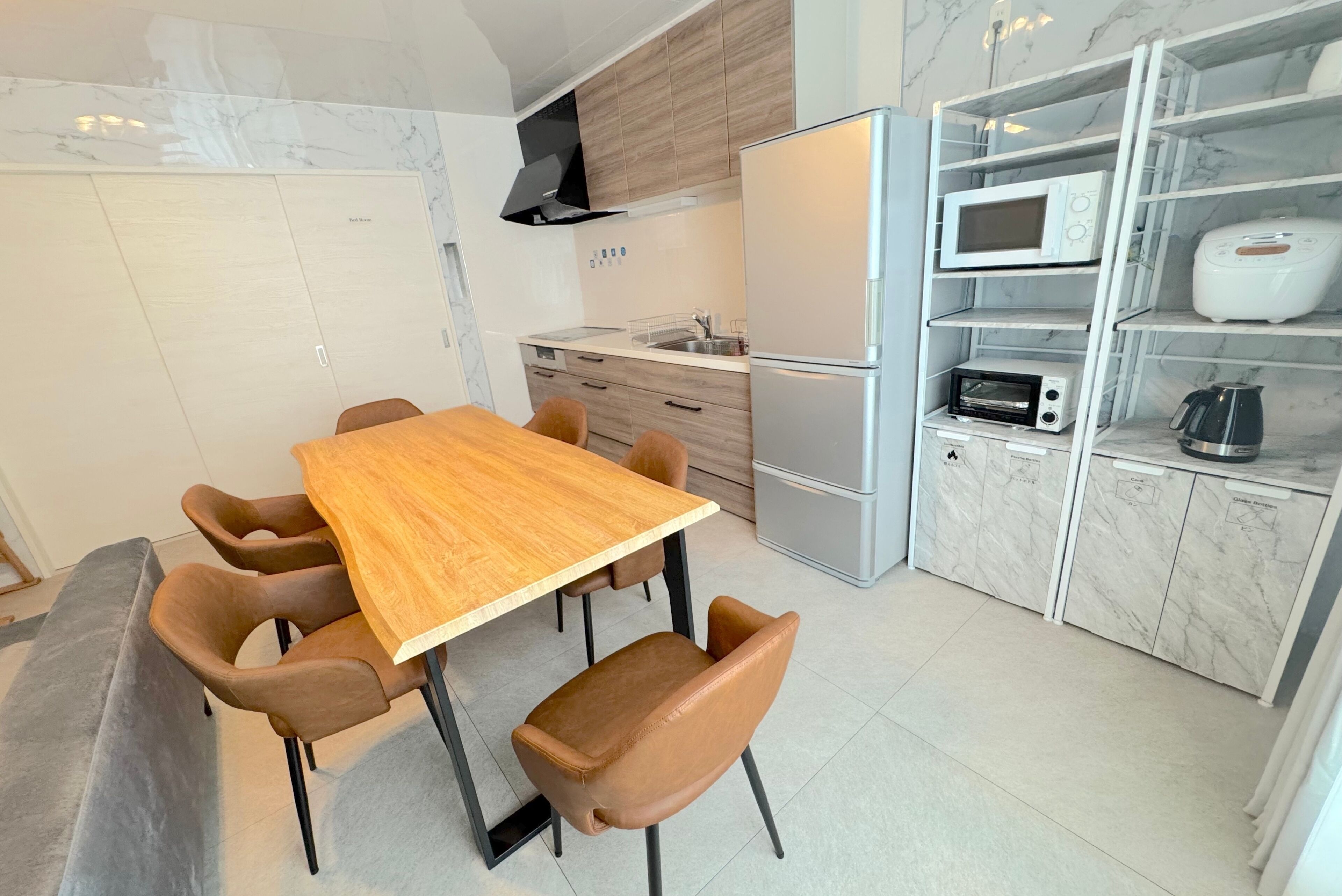 A modern kitchen with a wooden dining table, brown chairs, a built-in microwave, and a coffee machine.