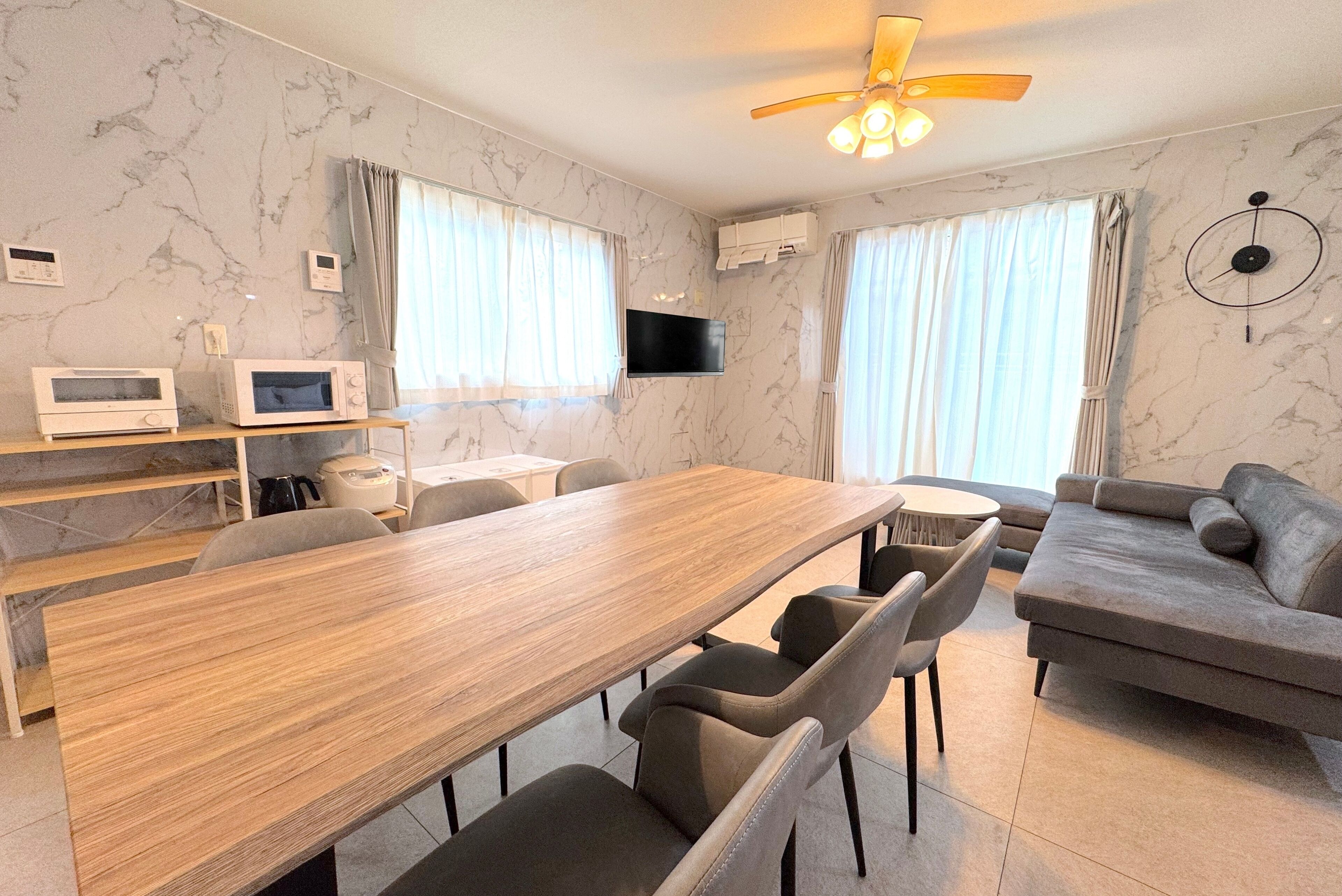 A modern living room with a wooden dining table, grey sofa, and a ceiling fan.
