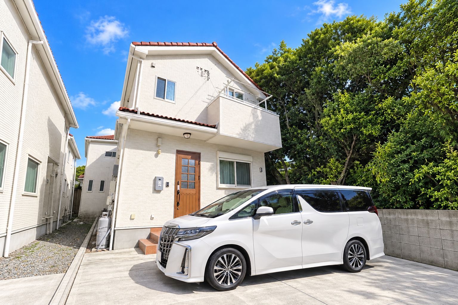 A white minivan parked in front of a two-story house with a red-tiled roof, a small front porch, and a paved driveway.