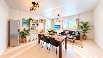 Une cuisine moderne dotée d’un four encastré, un coin repas avec une table et des chaises en bois, et un salon avec un canapé et un téléviseur.