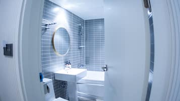 A modern bathroom with a white sink, a round mirror, and a bathtub.