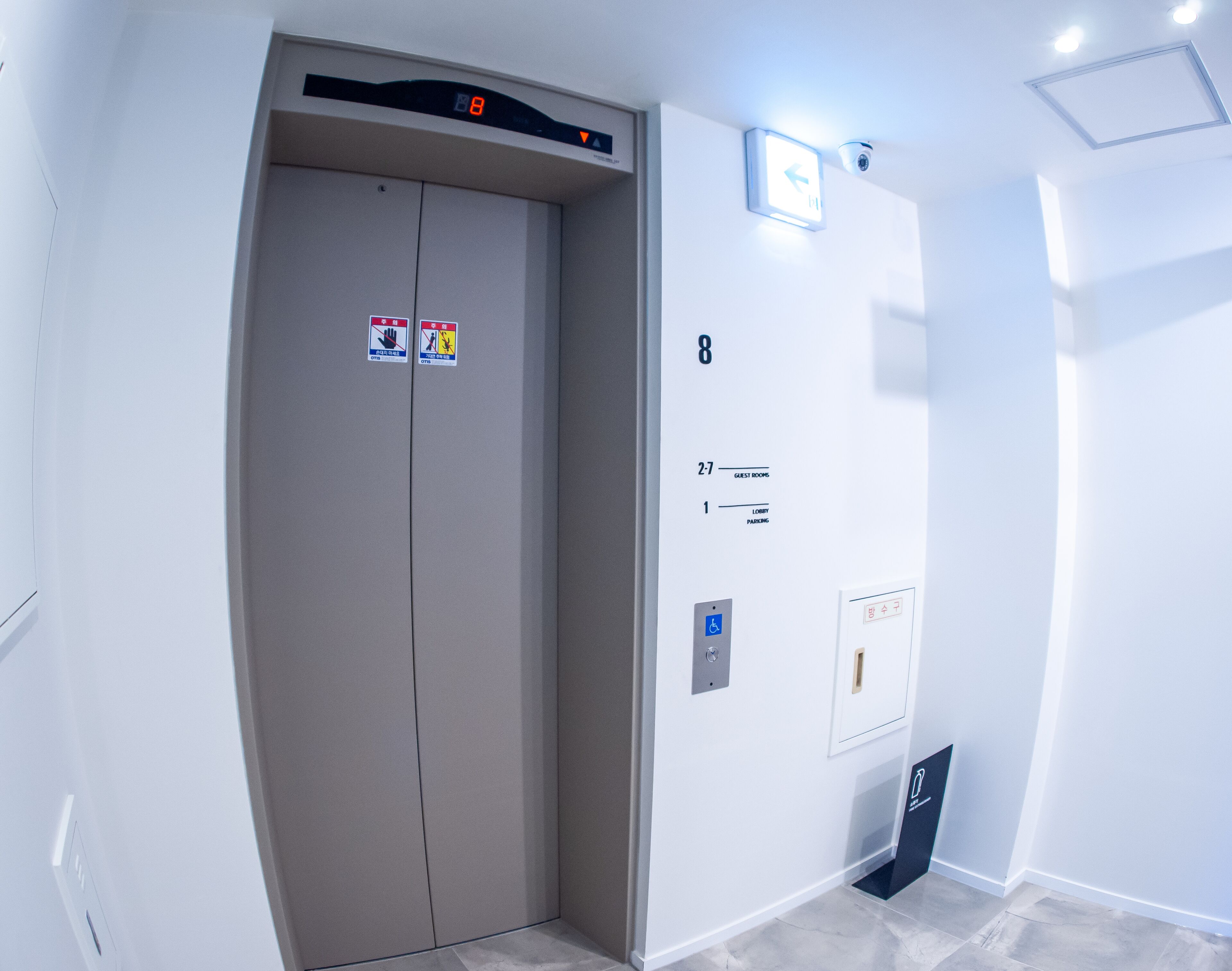 Un ascensor con pantalla digital, señal de salida de emergencia e indicador de piso.