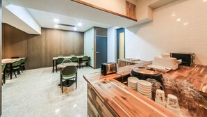 A modern dining area with wooden tables and chairs, a kitchen counter with appliances, and a view of the city through a large window. - Hotel  Yam YeonSan (Busan)