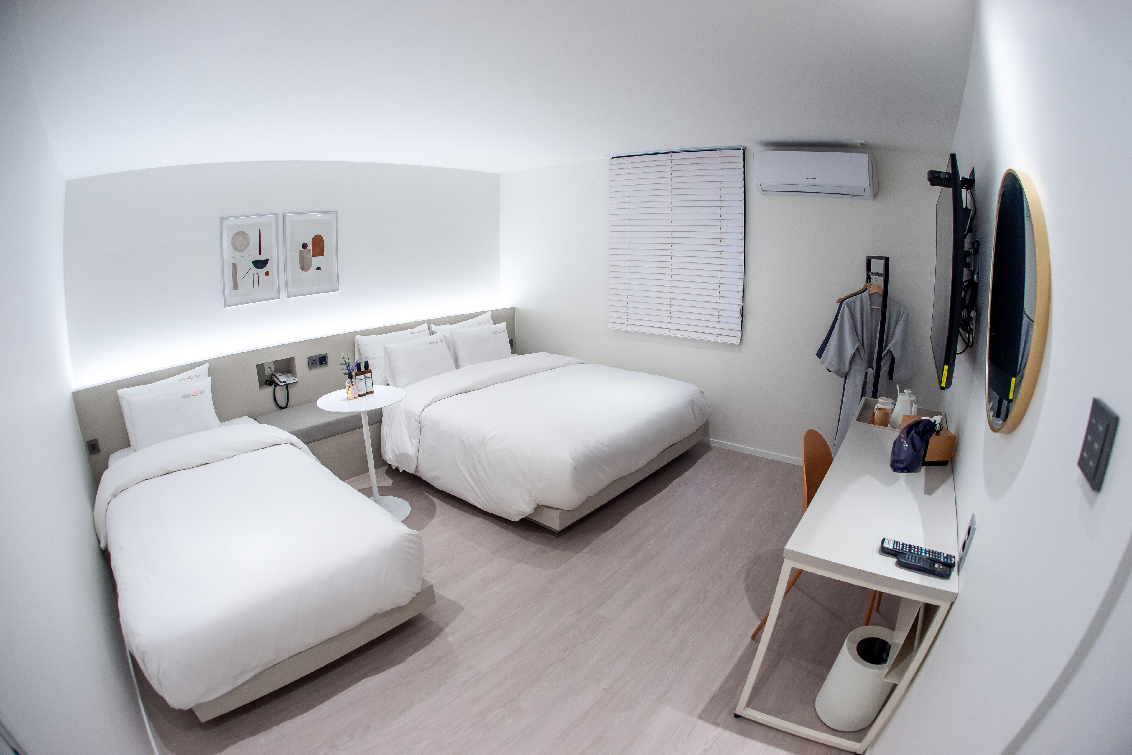 A modern hotel room with two beds, a small table, a desk, and a mirror.