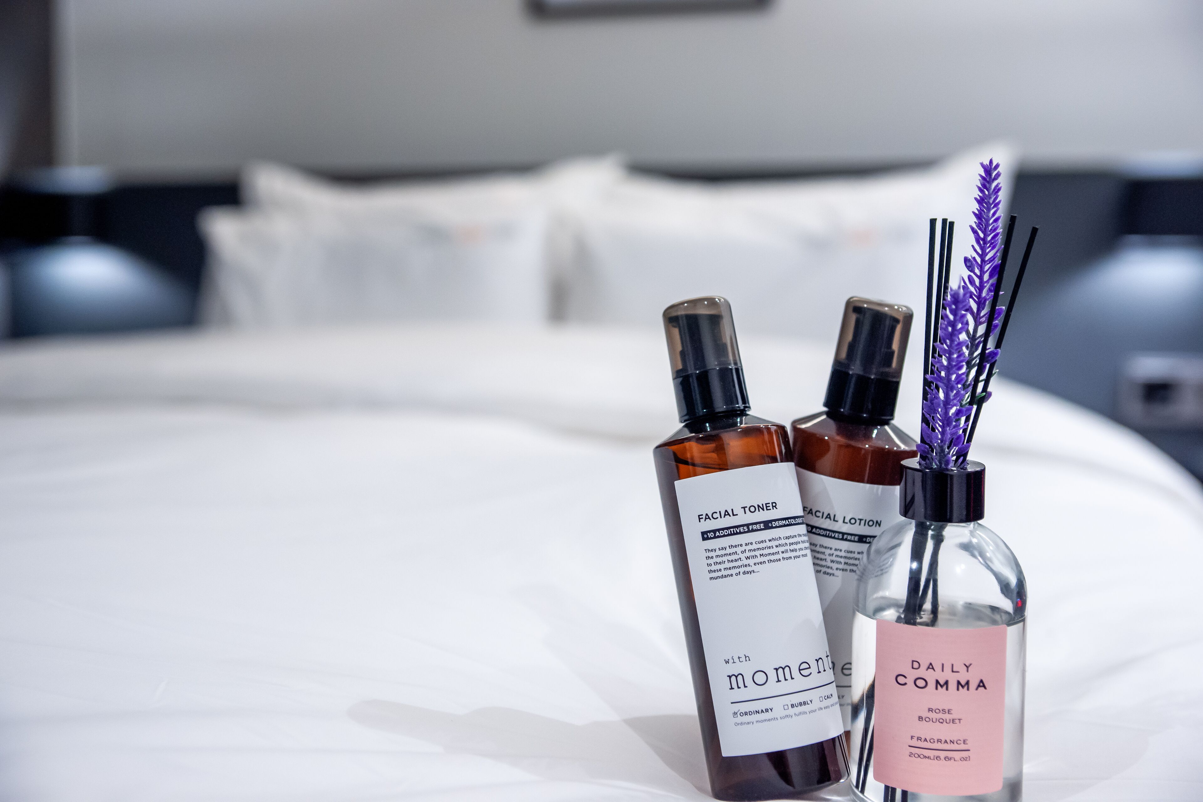 Un ensemble de produits de soins pour la peau, soigneusement disposés, sur une table de chevet avec une literie blanche et une tête de lit moderne.