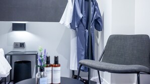 A modern hotel room with a grey chair, a black table with a lamp, and a clothing rack with hanging garments. - Hotel  Yam YeonSan (Busan)