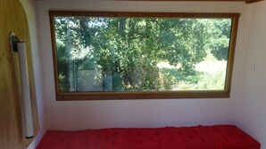 A room with a large window, a red bench, and wooden cabinets. - La pause Tiny: green relaxation in Morbihan (Ploërmel - (56800))