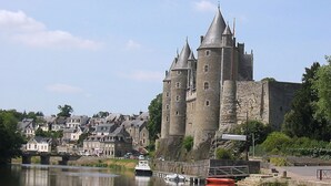 A historic castle with multiple towers and a moat, surrounded by residential buildings and a calm river. - La pause Tiny: green relaxation in Morbihan (Ploërmel - (56800))