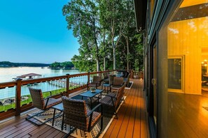 Eine Terrasse mit Gartenmöbeln, Blick auf einen See und ein Gebäudeeingang.