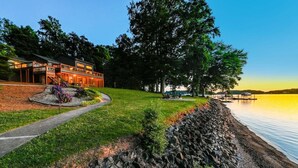 Une propriété au bord du lac, dotée d’un mur en pierre, d’un chemin menant à un bâtiment à la façade en verre et d’une jetée s’avançant dans l’eau.