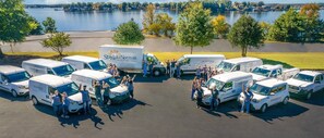 A group of people standing in front of multiple StayLakeNorman Luxury Vacation Homes vans parked in a lot with a lake and trees in the background. - Normandy Approach w/Optional Boat Rental (Mooresville)