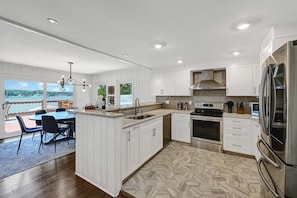 Una cocina moderna con armarios blancos, una isla grande, horno empotrado y vistas al exterior.