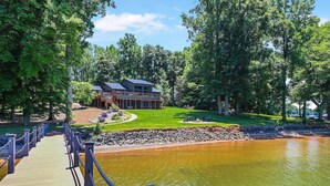 Un chalet au bord du lac, doté d’une terrasse en bois, d’un espace barbecue et d’un grand bâtiment également pourvu d’une terrasse.