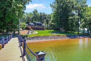 A lakeside lodge with a wooden deck, a fire pit area, and a large building with a deck. - Normandy Approach w/Optional Boat Rental (Mooresville)