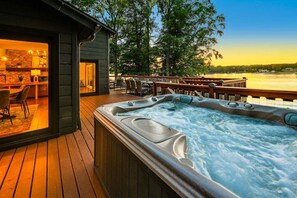 A hot tub on a wooden deck with a view of a body of water and a building with a glass door. - Normandy Approach w/Optional Boat Rental (Mooresville)
