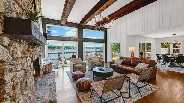 Un salon spacieux avec une cheminée en pierre, de grandes fenêtres et une vue sur un lac.
